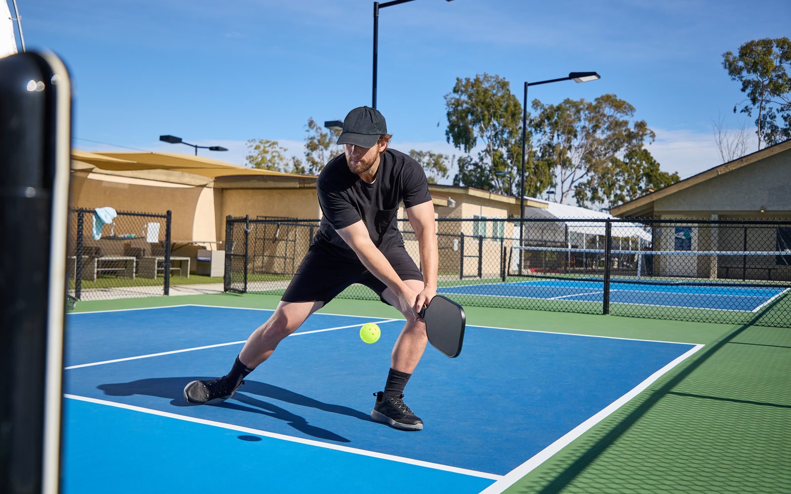 A player lunging wide to return a low ball on an outdoor blue pickleball court.