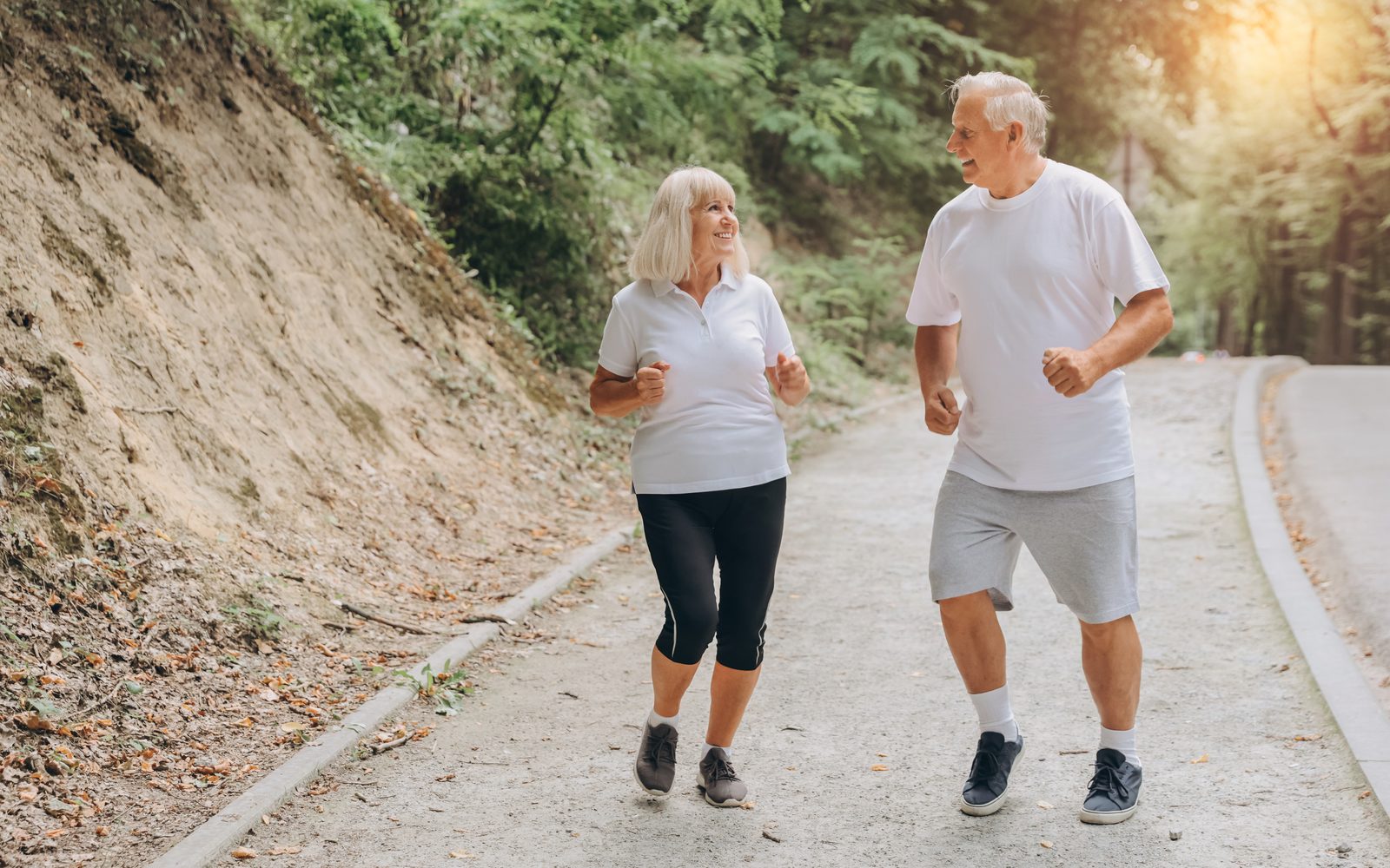 Two older adults jogging side by side along a shaded path in the morning.