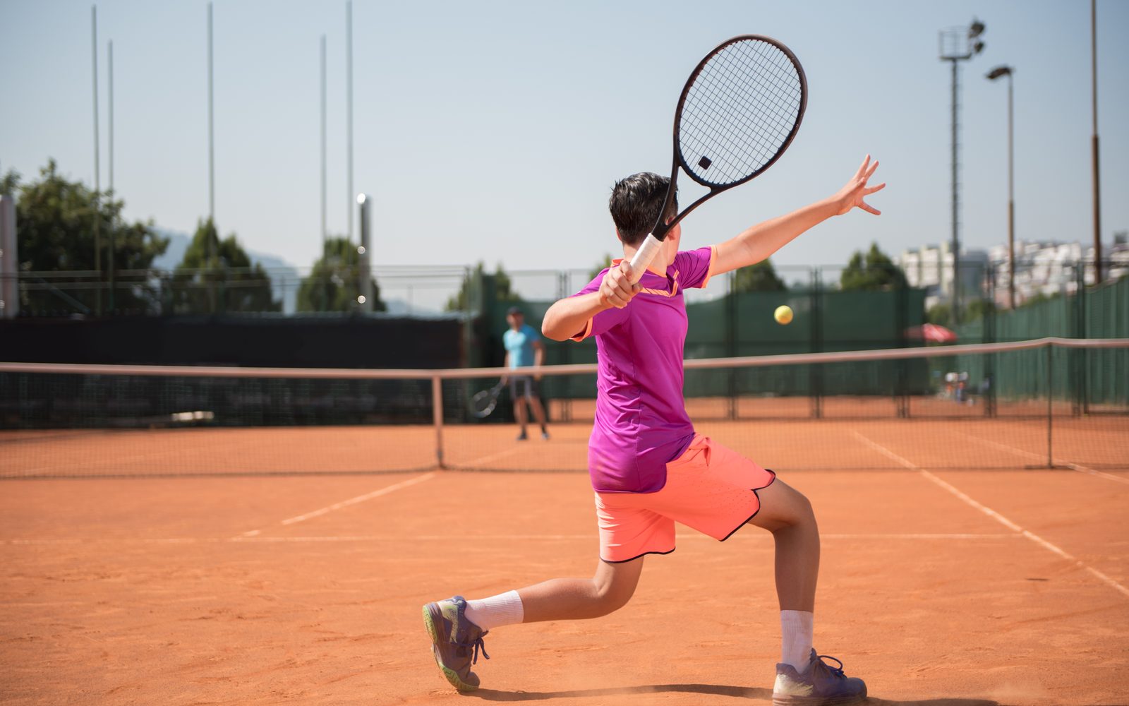 A tennis player stretched into a running forehand on a clay court.